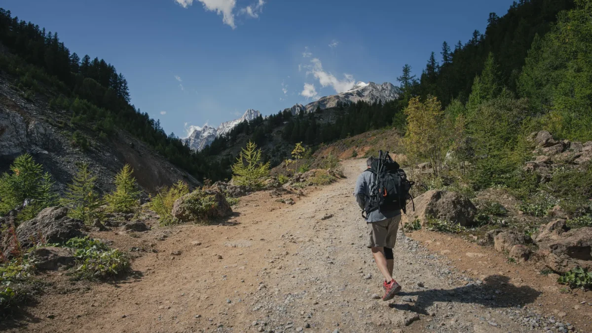 Lone hiker walking a scenic mountain trail under a clear blue sky