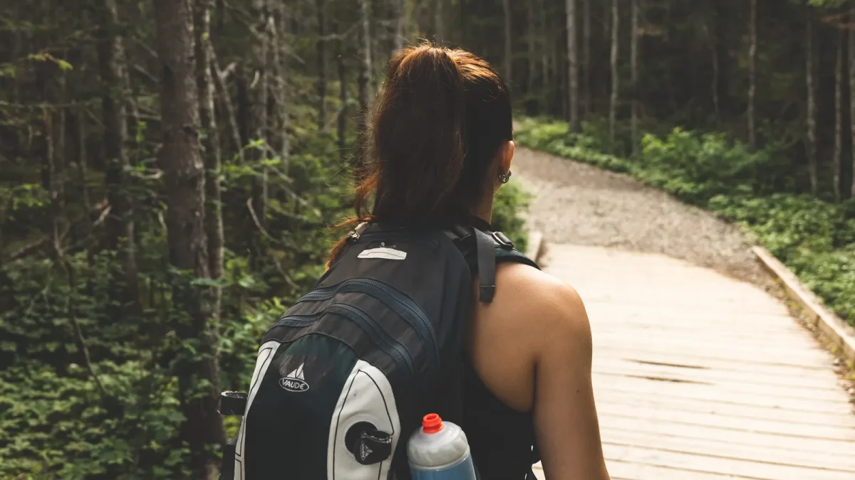 Back view of a woman hiking with a backpack on a wooden boardwalk trail