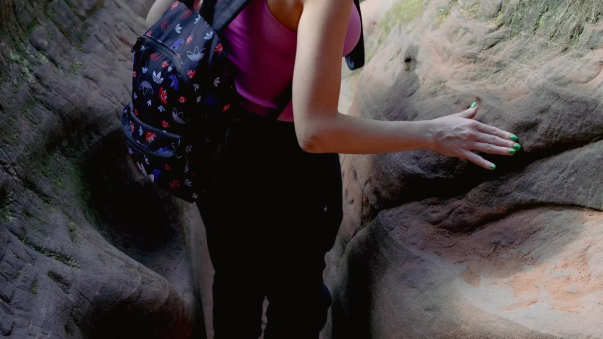 Woman in a tank top climbing over rocks with a small backpack