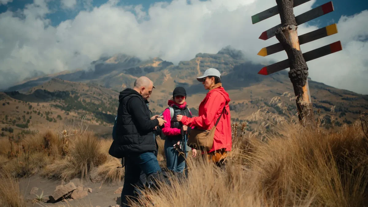 Hikers pausing at a mountain trail junction beside a wooden signpost