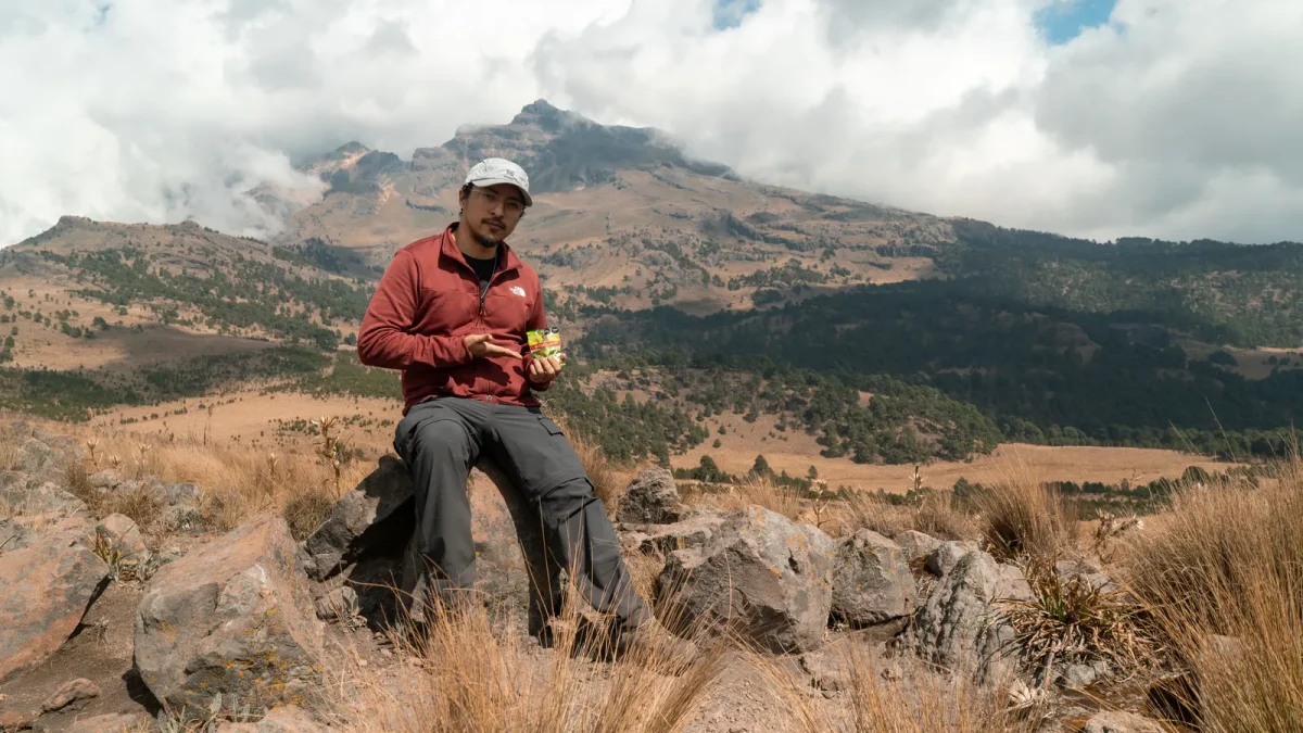 Man sitting on rocks eating a snack with a wide mountain view behind him