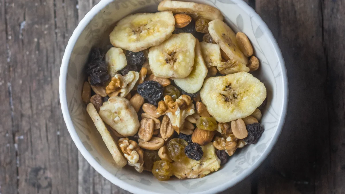 Bowl of mixed nuts and dried fruit including banana chips on a wooden table