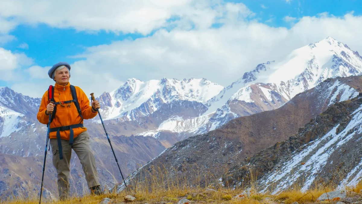Older woman hiking with trekking poles below snow-capped mountains